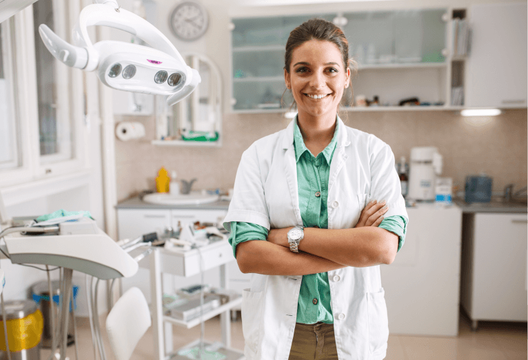 Smiling female dentist in clinic with arms crossed.