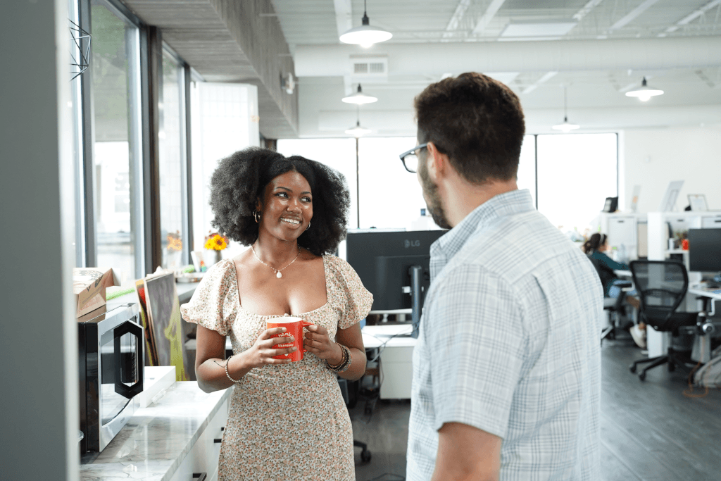 Two colleagues chatting with coffee in a bright office space